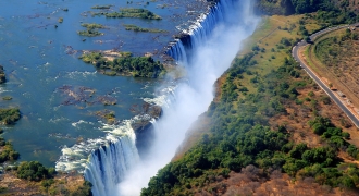 Image showing the stunning Victoria Falls, also known as 'The Smoke That Thunders', located on the border of Zambia and Zimbabwe. The waterfall's majestic waters cascade over the cliff, creating a breathtaking misty spray and vibrant rainbow in the sunlight.